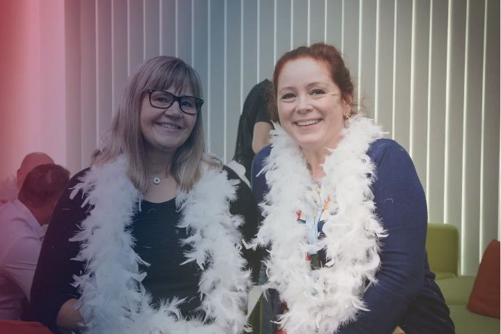two female consafe logistics employees with boa scarves smiling at the camera