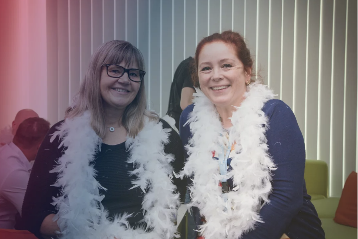 two female consafe logistics employees with boa scarves smiling at the camera two female consafe logistics employees with boa scarves smiling at the camera