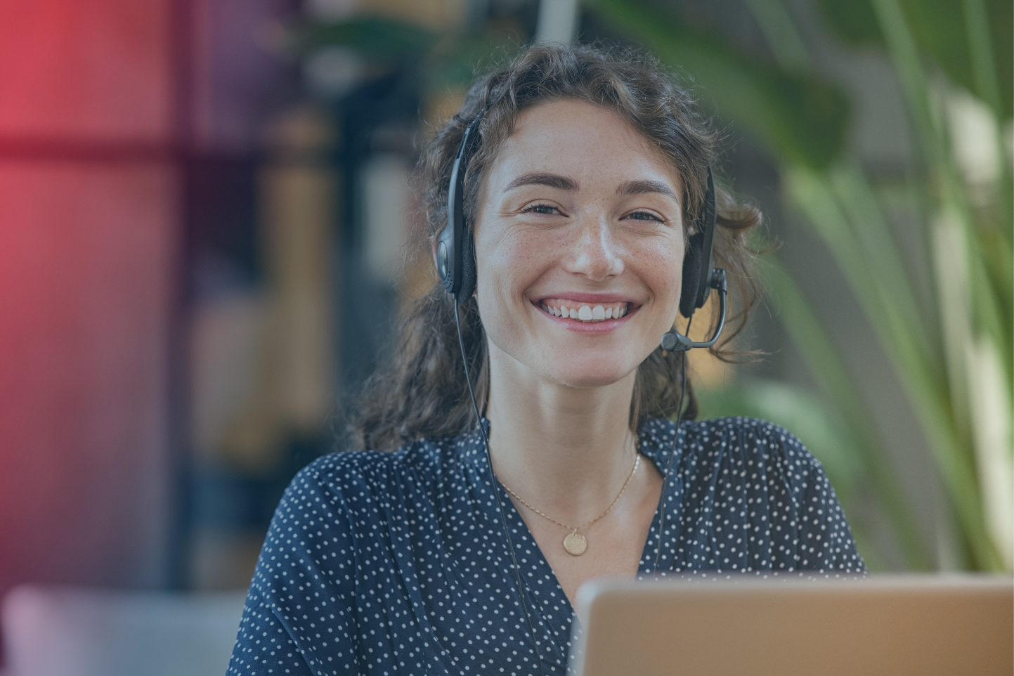 A customer service employee sits with a headset and smiles 