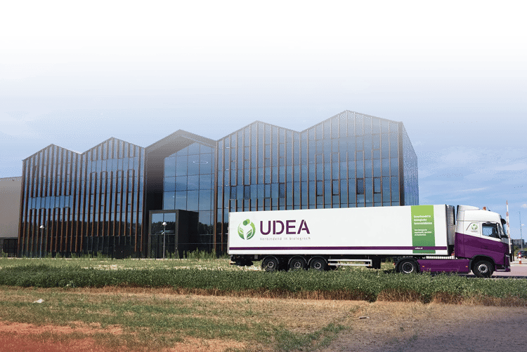 Udea logoed truck in white, purple, and green, parked outside their office with vibrant green grass and a clear blue sky