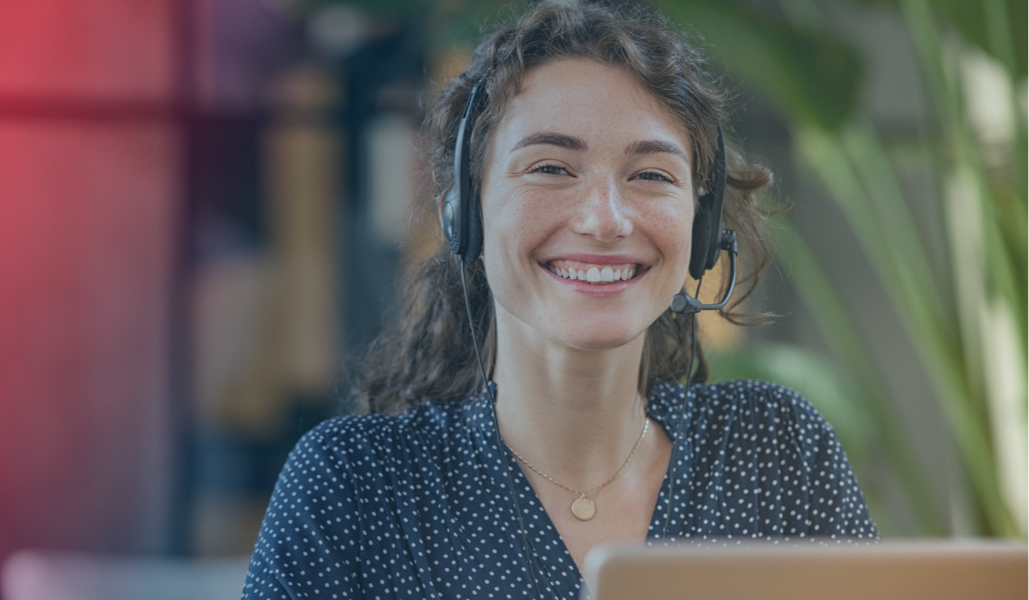 A customer service employee sits with a headset and smiles 