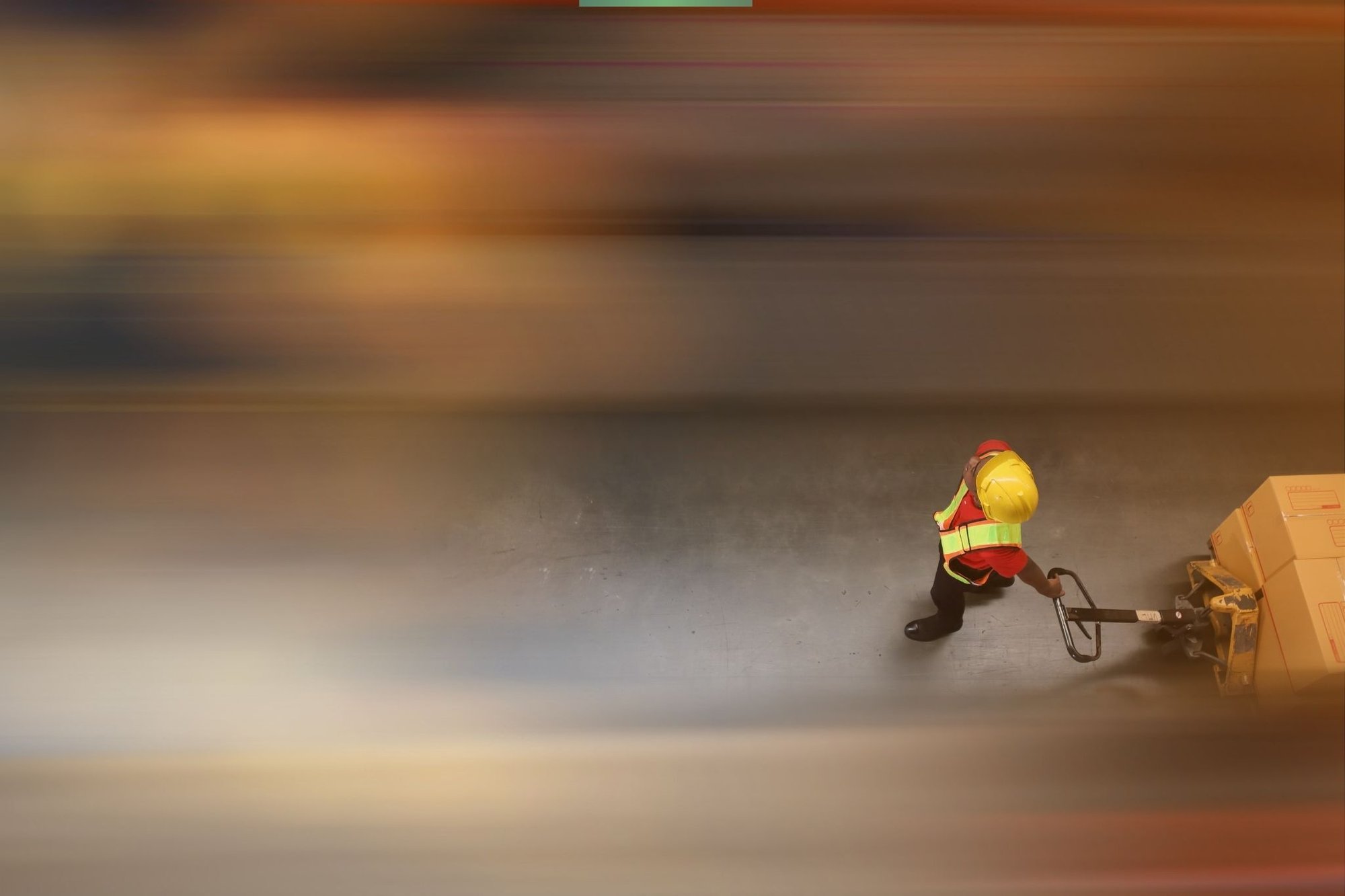 Warehouse worker in high-visibility clothing moving goods with a pallet jack, motion blur showing fast-paced warehouse operations.