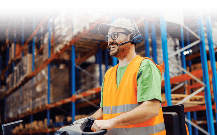 A warehouse worker drives a truck with a safety vest and headset on