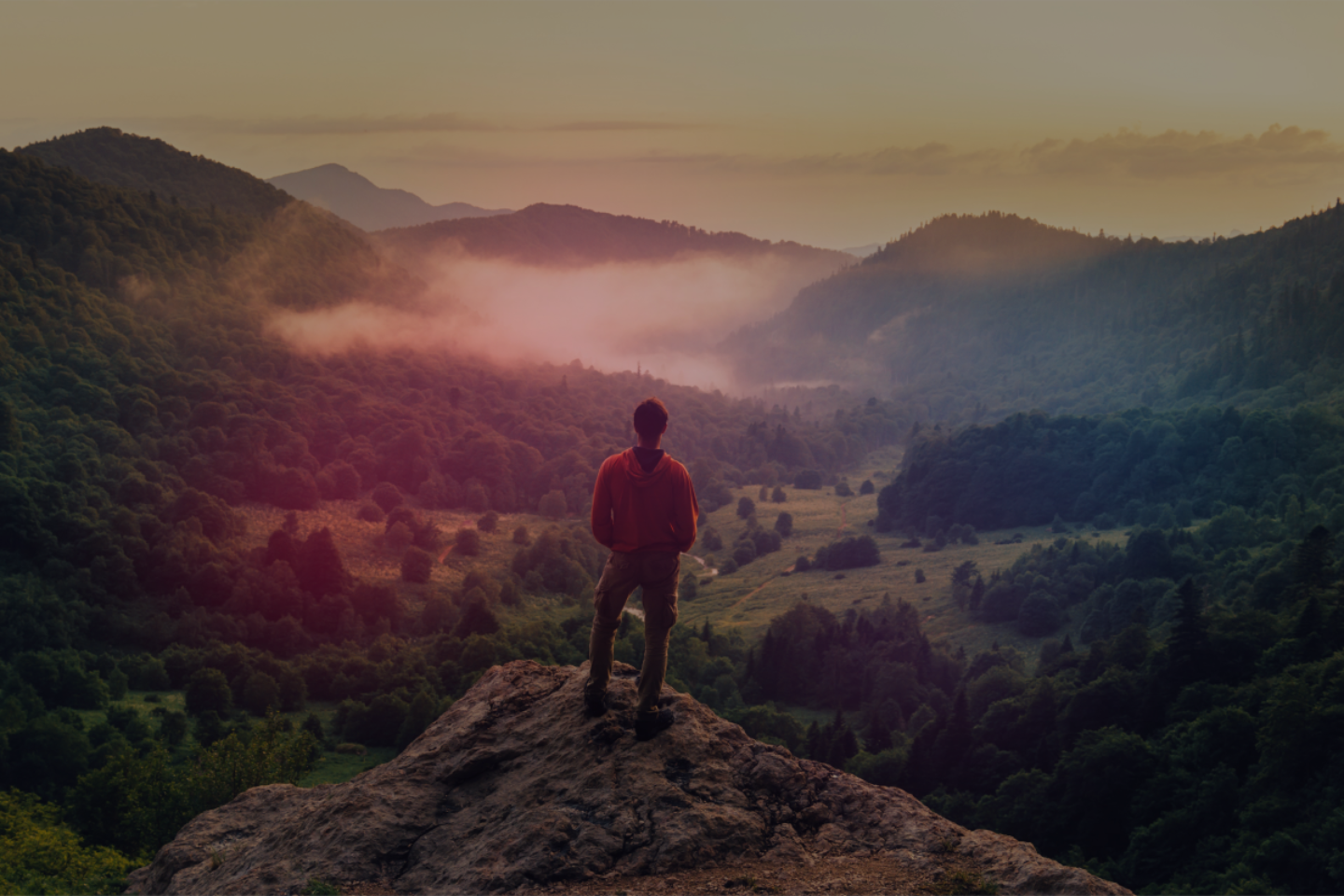 A person stands on a mountain and looks out over the landscape