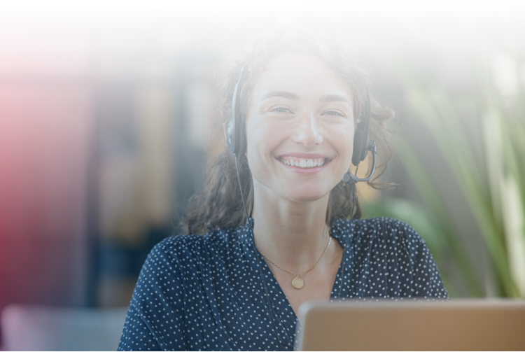 A customer service employee sits with a headset and smiles