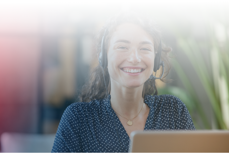 A customer service employee sits with a headset and smiles 