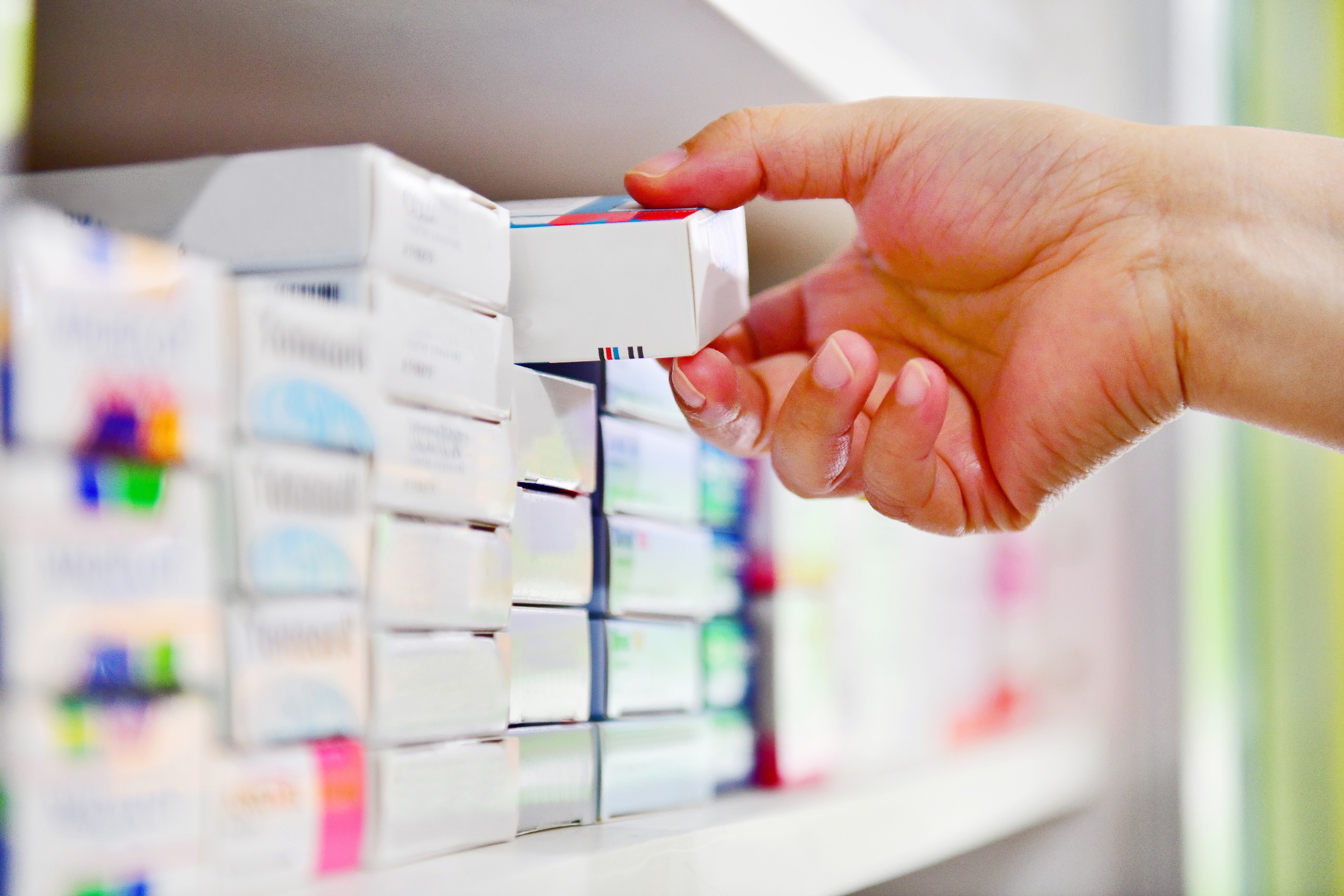 A hand reaching for a medicine box from a pharmacy shelf