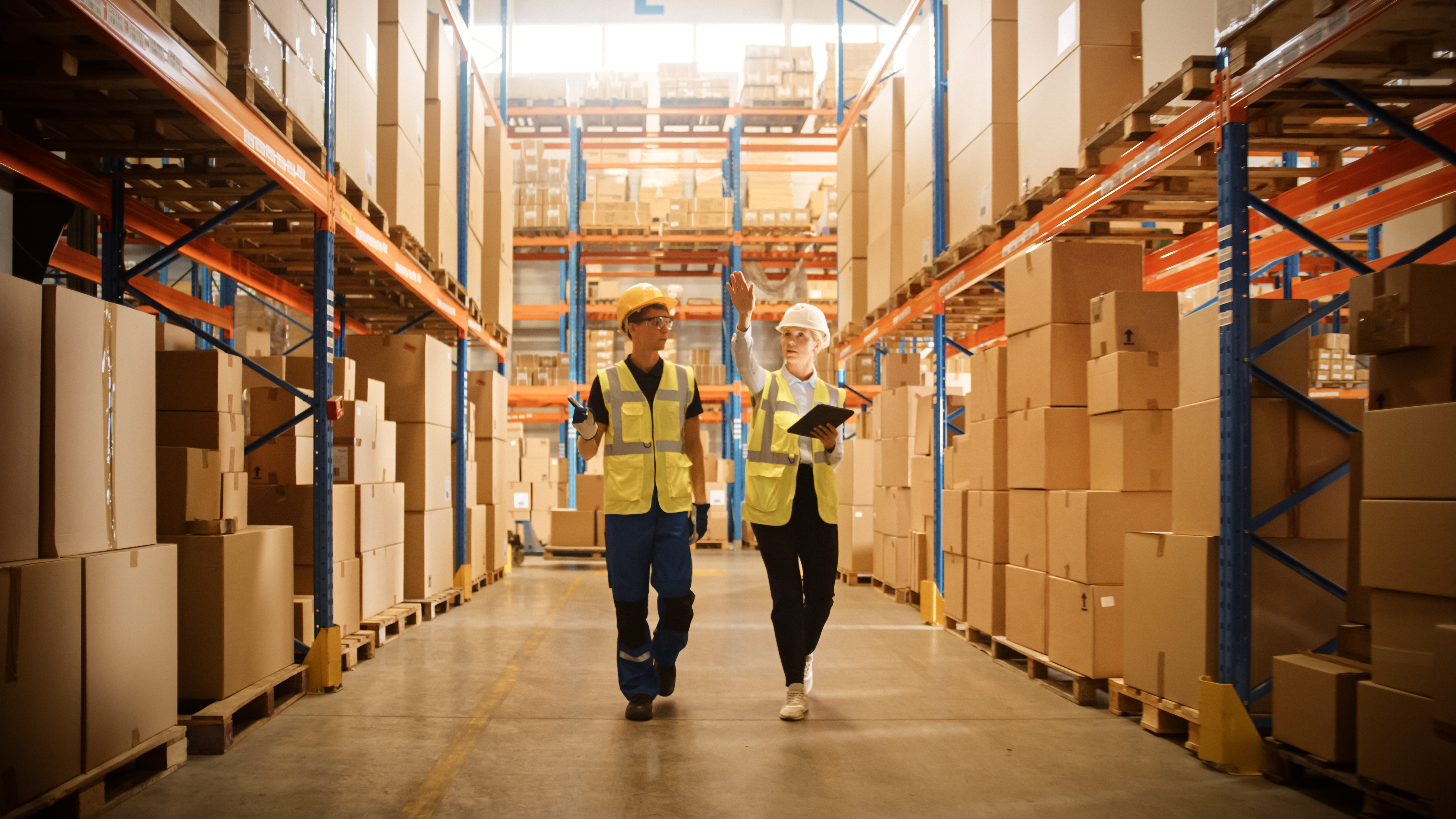 Male worker and female supervisor using a digital tablet to review warehouse layout and optimize warehouse space in a retail warehouse.