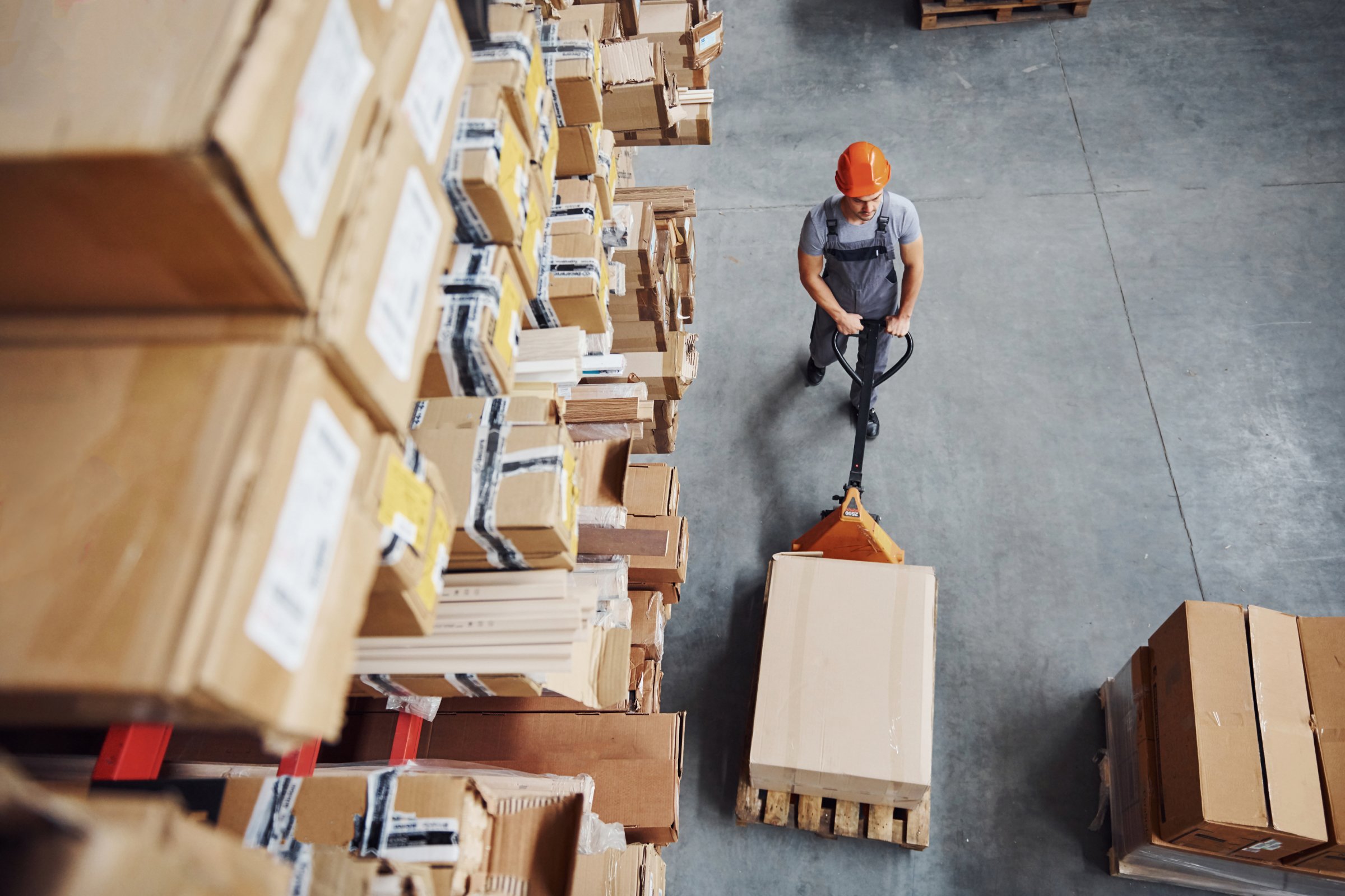 Top view of male worker in a warehouse doing a warehousing activity; pallet truck moving warehouse goods