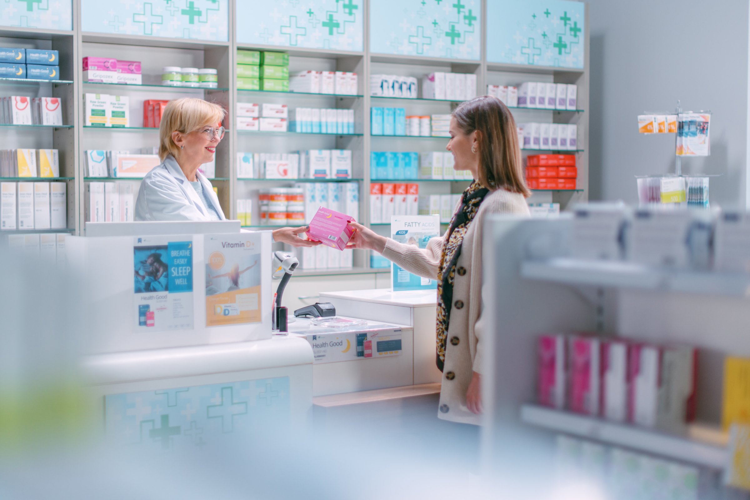 pharmacist hands over a pink package of medicine to the female buyer