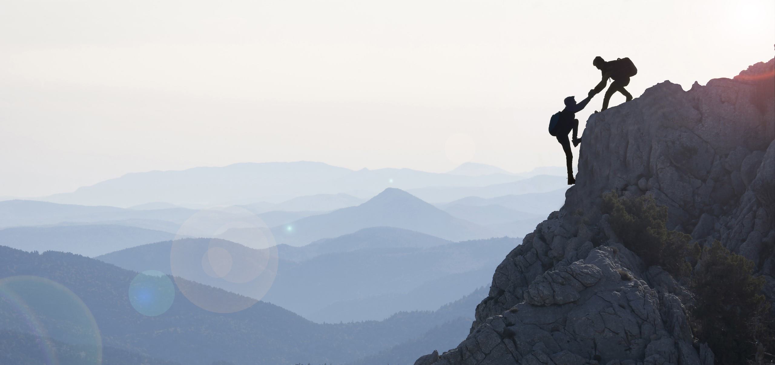 One person pulls another up the last bit of the mountain